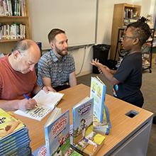 Image of authors signing book for student.